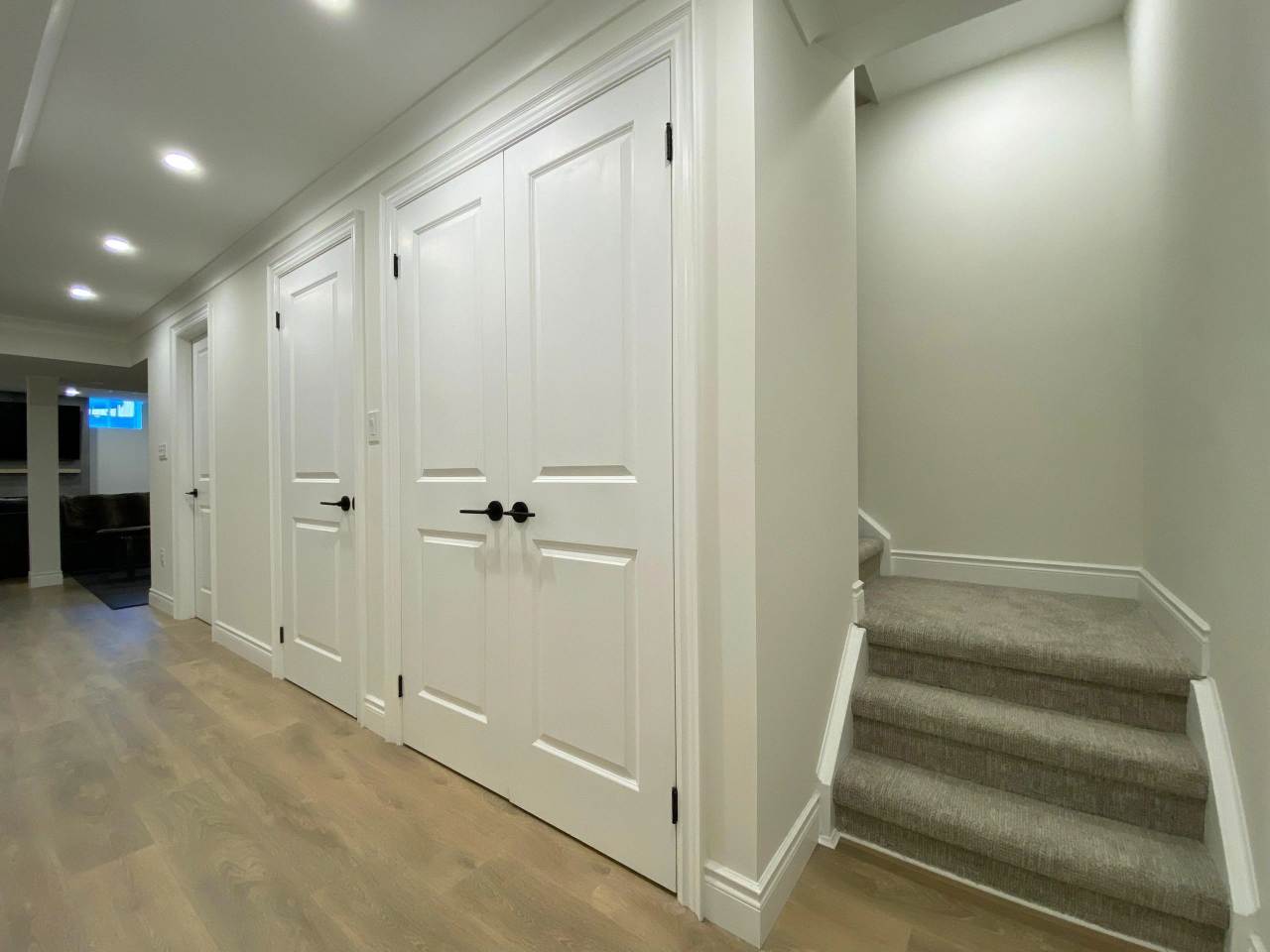 A hallway with white doors and stairs leading to the basement.